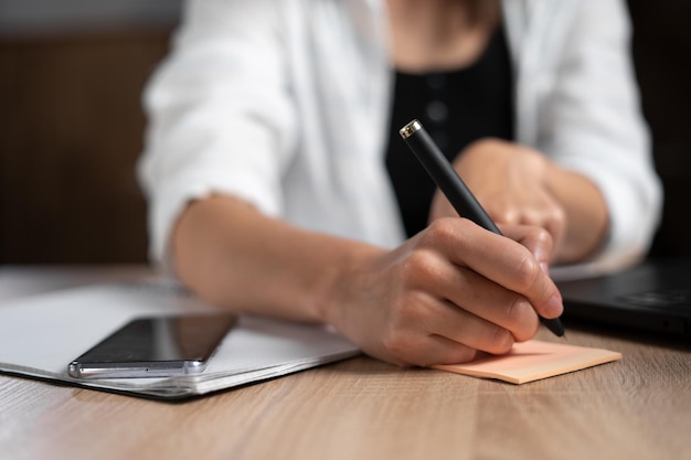 Mulher de negócios tomando notas enquanto trabalhava no escritório mão de mulher com uma caneta closeup o gerente está escrevendo algo escrito à mão na mesa negócios e trabalho