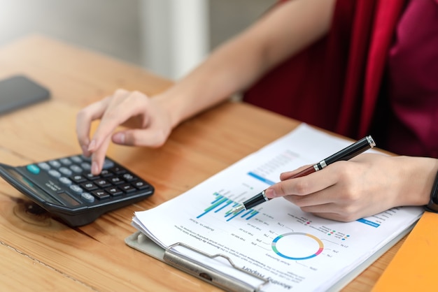 Mulher de negócios trabalhando no cálculo de estatísticas de receita do orçamento usando a calculadora, segurando uma caneta apontando para o gráfico no escritório.