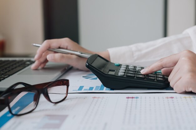 Mulher de negócios usando a calculadora e laptop para fazer finanças matemática na mesa de madeira no escritório