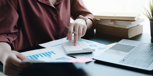 Mulher de negócios usando calculadora e laptop para fazer finanças matemáticas em uma mesa de madeira em