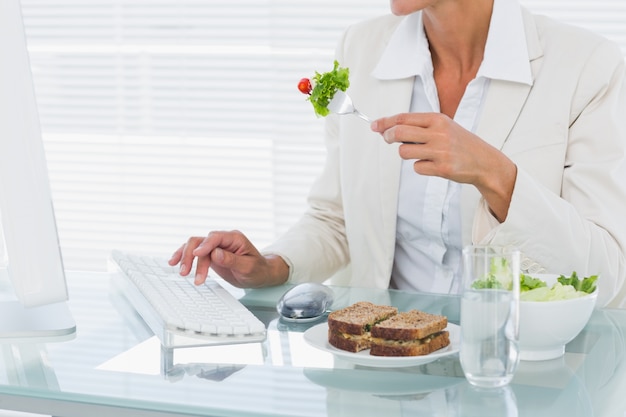 Mulher de negócios usando computador enquanto come salada na mesa
