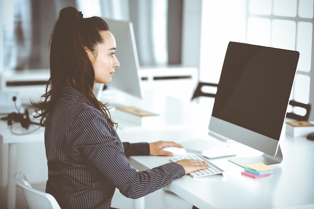 Mulher de negócios usando computador no local de trabalho no escritório moderno Secretária morena ou advogada sorrindo e parece feliz Trabalhando por prazer e sucesso