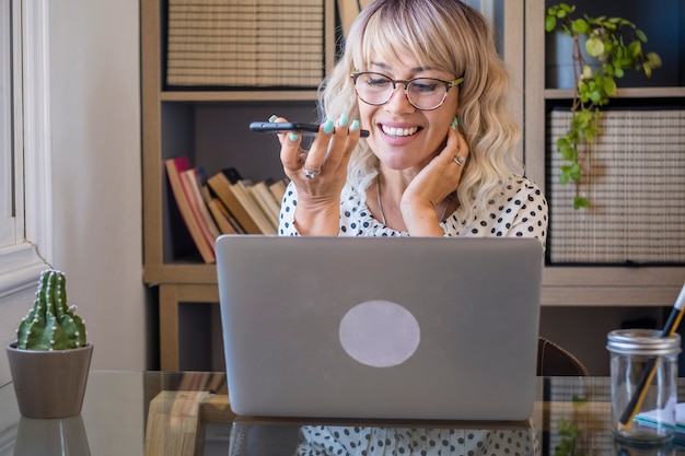 Mulher de negócios usando laptop enquanto fala no celular no escritório. mulher ocupada no trabalho. mulher falando no celular no escritório por meio de chamada de voz, alto-falante ou reconhecimento de fala.