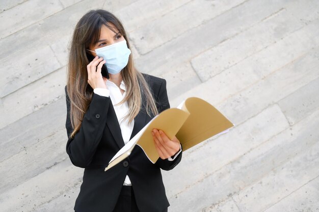 Foto mulher de negócios usando máscara falando ao telefone de pé contra a parede