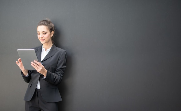 Mulher de negócios usando seu tablet na frente de uma parede preta semelhante a um quadro-negro