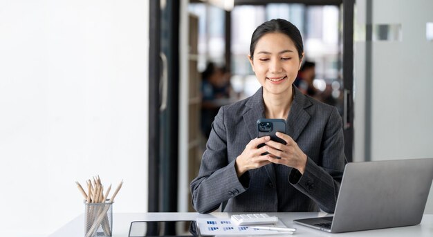 Mulher de negócios usando seu telefone no escritório Empreendedor de pequenas empresas olhando para seu telefone celular e sorrindo enquanto se comunica com seus colegas de escritório