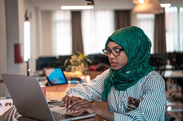 Mulher de negócios vestindo um hijab verde usando laptop na área de relaxamento no escritório de inicialização de plano aberto moderno. Foco seletivo. Foto de alta qualidade