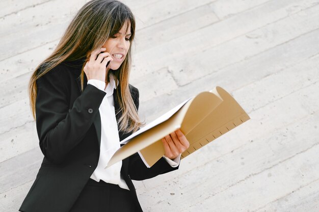 Mulher de negócios zangada segurando documentos e gritando ao telefone