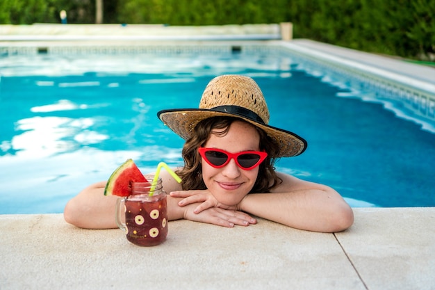 Foto mulher de óculos, aproveitando o sol na piscina jovem garota tomando um coquetel nas férias de verão