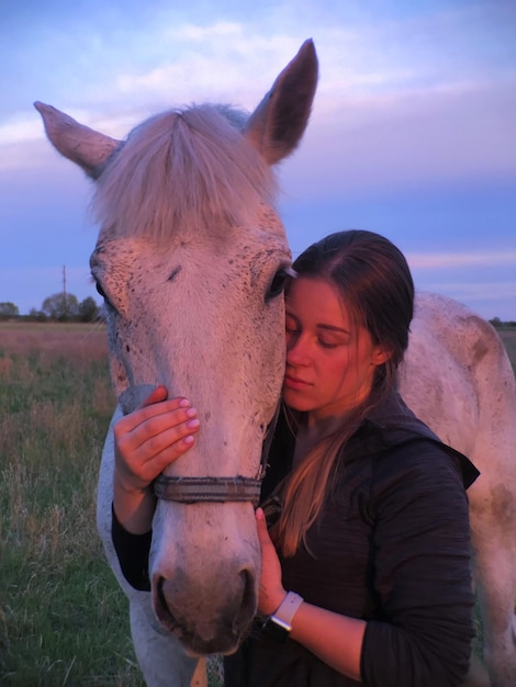 Foto mulher de pé ao lado de um cavalo no campo contra o céu