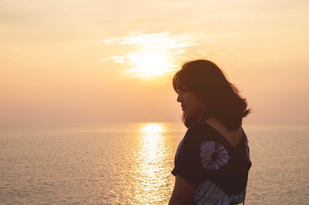 Mulher de pé contra o mar e o céu durante o pôr do sol