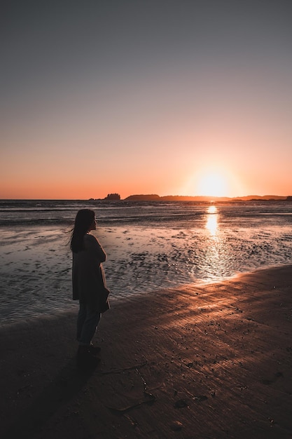 Mulher de pé na praia durante o pôr do sol