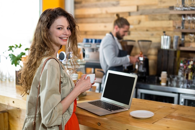 Mulher de pé no balcão e usando o laptop enquanto tomando café no café