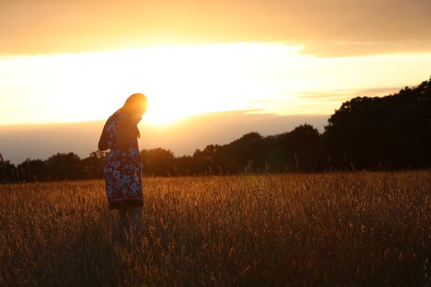 Foto mulher de pé no campo contra o céu durante o pôr do sol