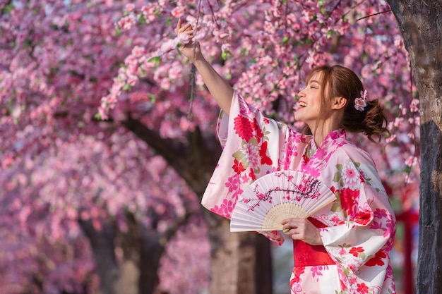 Foto mulher de pé perto de uma cerejeira rosa em flor