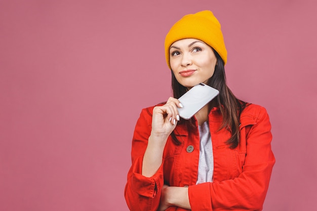 Mulher de pensamento segurando o telefone. Foto da jovem mulher bonita bonito alegre que conversa pelo telefone móvel isolado sobre a parede cor-de-rosa da parede.