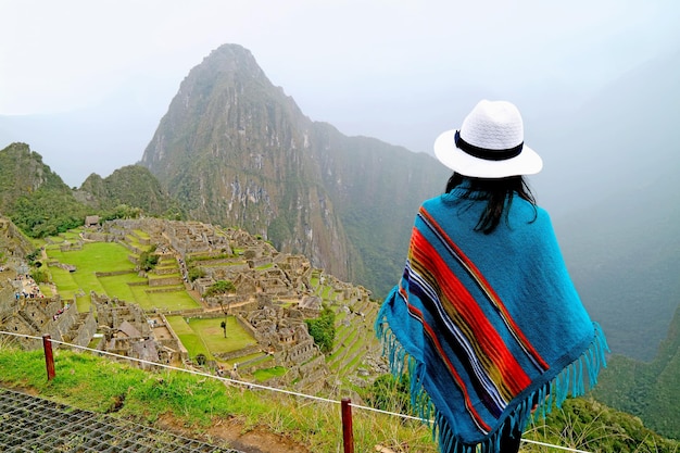 Mulher de poncho azul sendo impressionada pela antiga cidadela inca de Machu Picchu no Peru