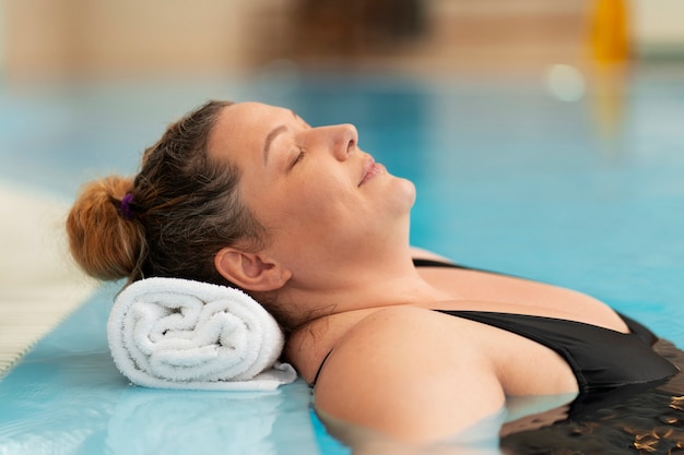 Foto mulher de porte médio a relaxar na piscina.