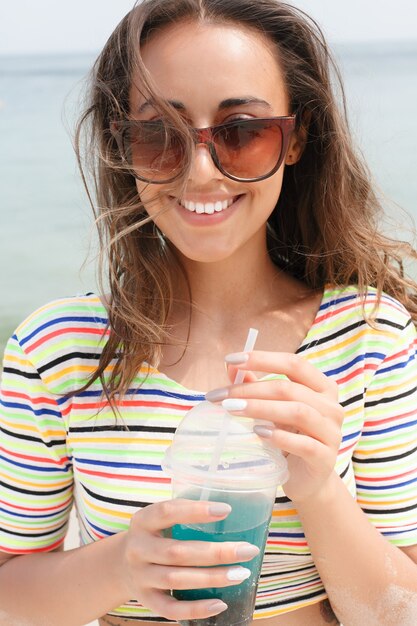 Mulher de praia bebendo bebida gelada, se divertindo na festa na praia. gata de biquíni, desfrutando de chá gelado, coca ou bebida alcoólica, sorrindo feliz rindo olhando para a câmera. linda garota mestiça