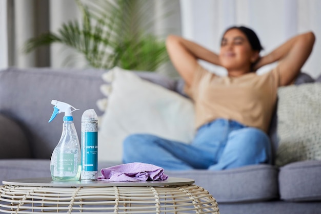 Mulher de produto de limpeza e sofá para relaxar, descansar ou dormir para trabalhos domésticos na sala de estar com alívio sofá de limpeza feliz com pano de spray e garrafa na mesa para trabalho de serviço e higiene