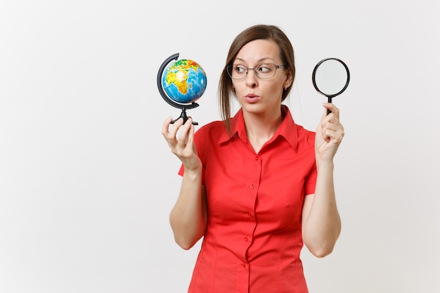 Mulher de professor de negócios atônito de camisa vermelha, segurando e olhando através de uma lupa no globo isolado no fundo branco. ensino de educação no conceito de universidade do ensino médio. copie o espaço.