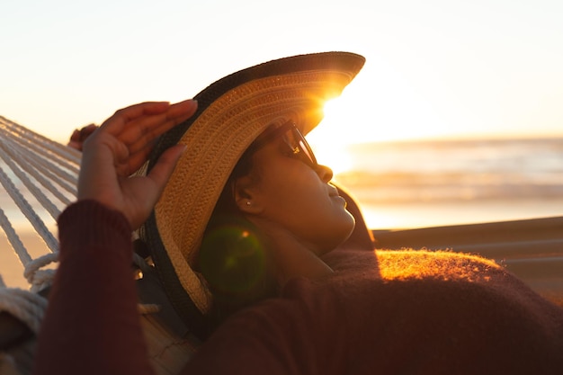 Foto mulher de raça mista em férias na praia deitada na rede relaxando durante o pôr do sol. tempo de lazer saudável ao ar livre à beira-mar.