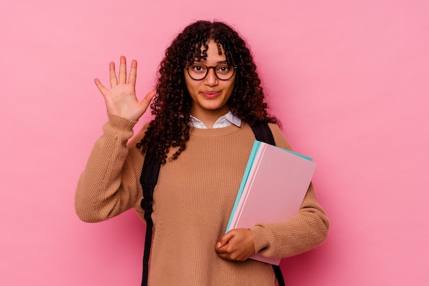 Mulher de raça mista jovem estudante isolada em rosa sorrindo alegre mostrando o número cinco com os dedos.