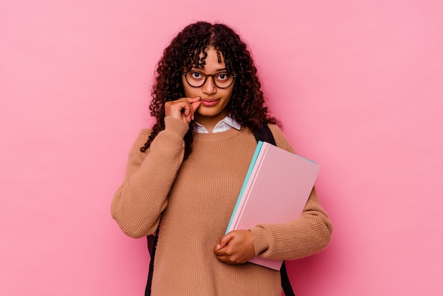 Mulher de raça mista jovem estudante isolada em um fundo rosa com os dedos nos lábios, mantendo um segredo.