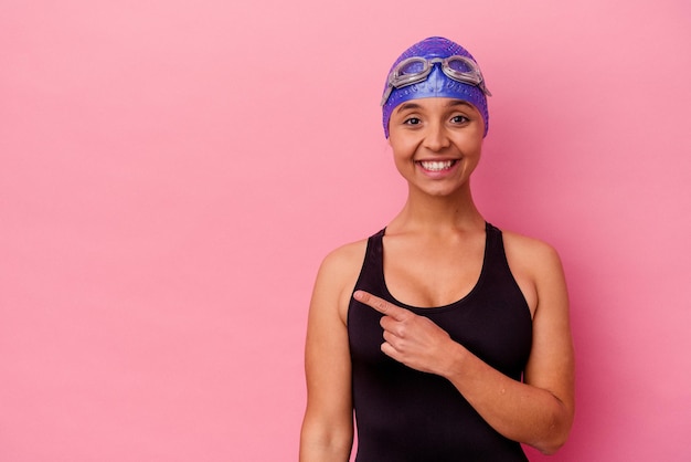 Mulher de raça mista jovem nadador isolada em fundo rosa sorrindo e apontando de lado, mostrando algo no espaço em branco.