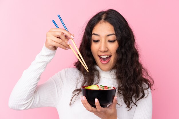 Foto mulher de raça mista, segurando uma tigela cheia de macarrão sobre parede rosa isolada