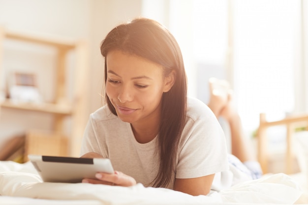 Mulher de raça mista usando Tablet na cama