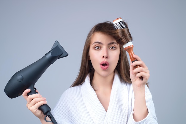 Mulher de roupão penteando cabelo secando com secador de cabelo retrato de modelo feminino com uma escova de pente
