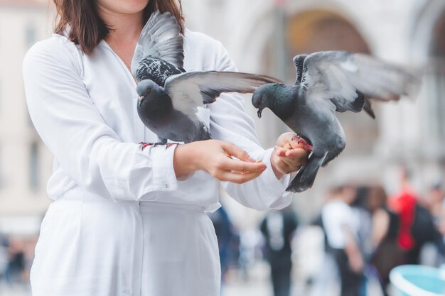 Mulher de roupas brancas com chapéu de palha se divertindo com pombos na praça da cidade de veneza