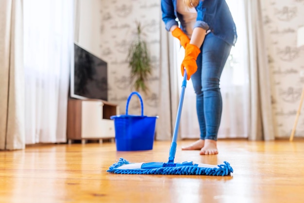 Mulher de roupas casuais lavando um chão de madeira com um esfregão de microfibra úmido