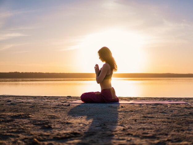 Foto mulher de silhueta na praia ao pôr do sol fazendo ioga asana. treino de alongamento natural matinal de aquecimento