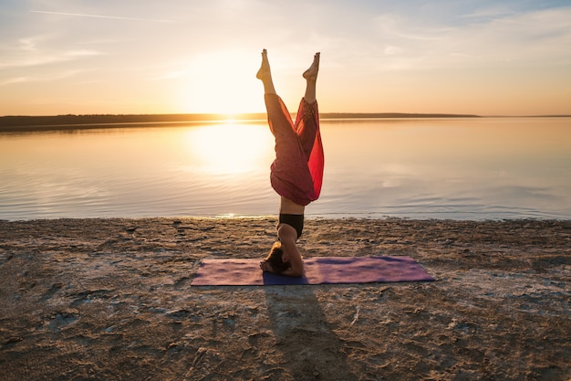 Foto mulher de silhueta na praia ao pôr do sol fazendo ioga asana. treino de alongamento natural matinal de aquecimento