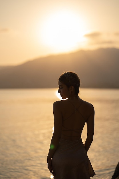 Mulher de silhueta usando vestido curto de glitter, aproveitando o momento romântico do pôr do sol na praia.