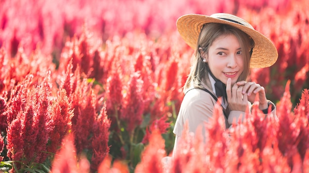 Mulher de sobretudo e chapéu de palha no campo de flores vermelhas.