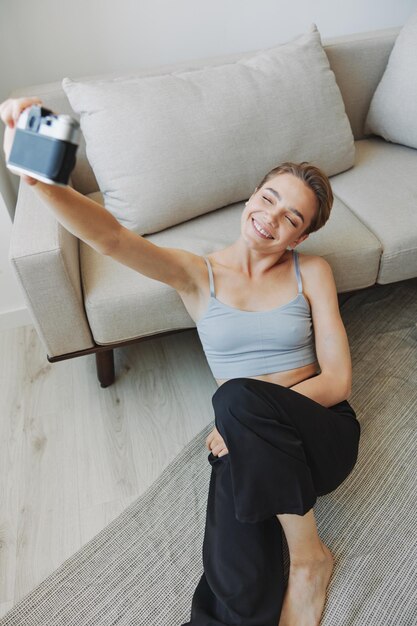 Mulher de sorriso feliz segurando uma câmera velha e tirando fotos de si mesma como uma fotógrafa de fim de semana em roupas caseiras com um corte de cabelo curto sem filtros em um espaço de cópia gratuita de fundo branco