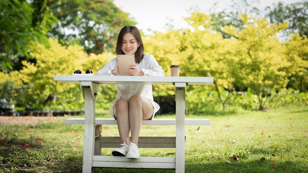 Mulher de sorriso pensativo no parque usando tablet digital inteligente Retrato de um jovem negócio encantador