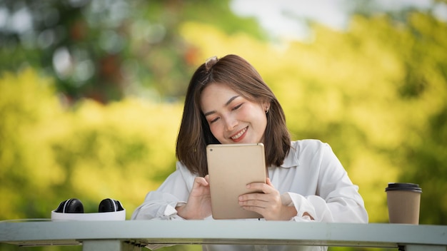 Mulher de sorriso pensativo no parque usando tablet digital inteligente Retrato de um jovem negócio encantador