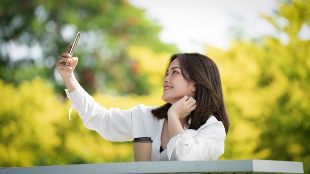 Mulher de sorriso pensativo no parque usando telefone inteligente para foto selfie Retrato de um jovem