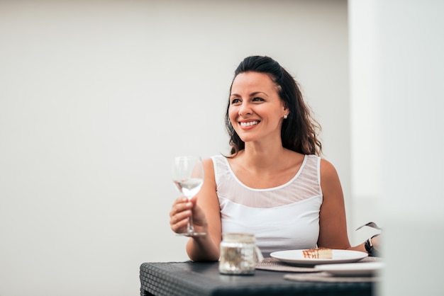 Mulher de sorriso que bebe um vidro do vinho e que come um bolo. fechar-se.