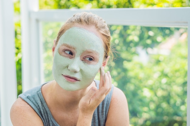 Mulher de spa aplicando máscara facial de argila verde tratamentos de beleza closeup retrato de menina bonita