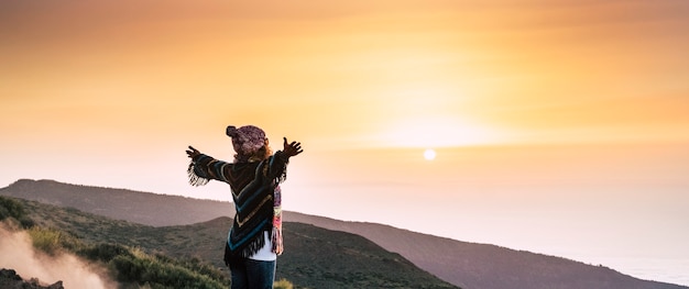 Mulher de sucesso no topo do mundo abre os braços e abraça um lindo pôr do sol colorido à sua frente