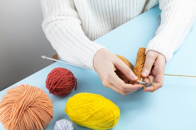 Mulher de suéter branco tricotando roupas de fio amarelo