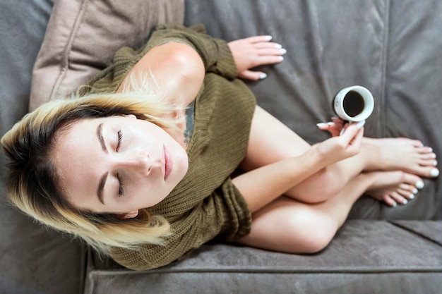 Mulher de suéter tomando café no sofá, fundo desfocado, vista superior