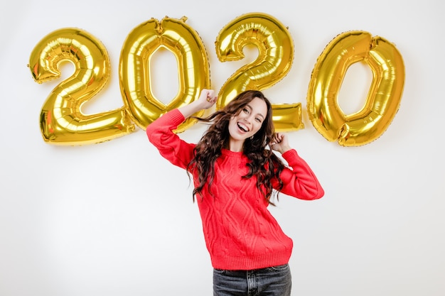 Mulher de suéter vermelho dançando na frente de balões de ano novo em 2020