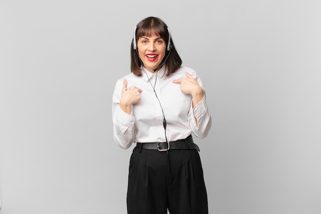 mulher de telemarketing se sentindo feliz, surpresa e orgulhosa, apontando para si mesma com um olhar animado e surpreso