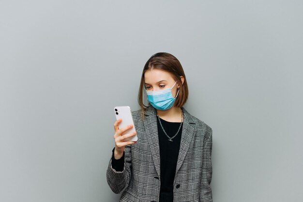mulher de terno cinza e uma máscara médica no rosto usa um smartphone com uma cara séria